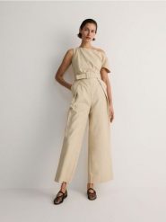 Kombinezon z paskiem - beżowy. Brązowe kombinezony damskie Reserved, l, bez wzorów, z bawełny, bez kołnierzyka, bez ramiączek. W wyprzedaży za 89.99 zł.